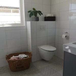 Fräscht badrum med inkaklad vägghängd toalett, vitt kakel och vackert mönstrat klinkergolv. Renoverat med säker plattsättning i Varberg.