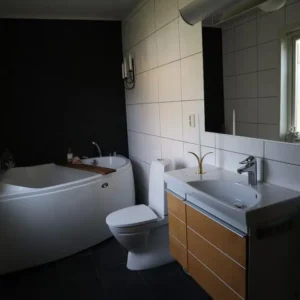 Nyrenoverat badrum i Varberg med hörnbadkar, vit toalett och snygg kommod med trälådor. Utfört av Byggtjänst i Träslöv AB.