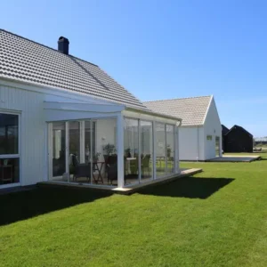 Stilrent och modernt uterum med pulpettak och glaspartier, byggt som en elegant förlängning av en vit villa i Varberg.
