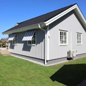 Ljusgrå villa med nymonterad stående träpanel, vita foder och fönstermarkiser, ett nyligen utfört fasadbyte.