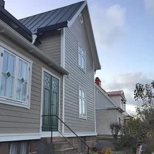 Grå trävilla i Varberg med nyrenoverad träfasad, vita foder och mörkgröna dubbeldörrar.