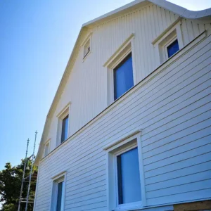 Vit trävilla med nymålad stående träpanel och nya foder under en pågående fasadrenovering.