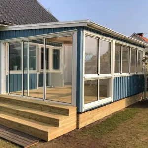 Ett vitt, platsbyggt uterum med glaspartier som smälter in perfekt mot den blå träfasaden på en villa.