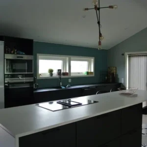Modernt svart kök med en rymlig vit köksö och stilrena gröna väggar, ett resultat av en professionell köksrenovering i Varberg.