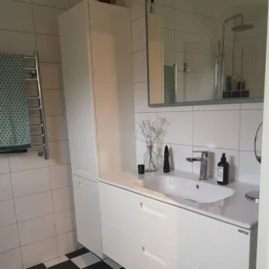 Ljust badrum med schackrutigt golv, handdukstork och montering av vit kommod samt högskåp. Professionell badrumsrenovering i Varberg.