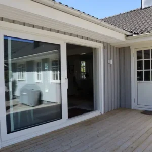 Nyinstallerad modern skjutdörr i glas bredvid en vit ytterdörr på en grå träfasad i Varberg.