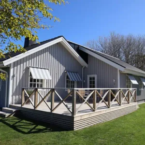 Nybyggt rymligt trädäck med ett klassiskt kryss-staket i trä, anpassat efter en grå villa i Varberg.