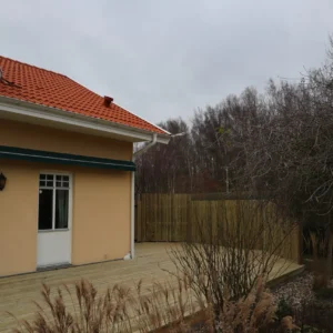Platsbyggd altan och trädäck som löper runt knuten på en gul villa, komplett med insynsskyddande trästaket i bakgrunden.