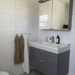 Stilrent och fuktsäkert badrum med grå kommod, spegelskåp och klassiskt vitt kakel. Totalentreprenad av våtrum i Varberg.