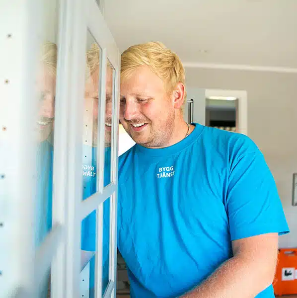 En glad och erfaren snickare från Byggtjänst i Träslöv klädd i arbetskläder, som utför ett byggprojekt i Varberg.