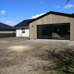 Exteriör på en snygg tillbyggnad med omålad, naturfärgad träpanel och svart tak. Ett byggprojekt utfört av Byggtjänst i Träslöv AB, din byggfirma i Varberg.